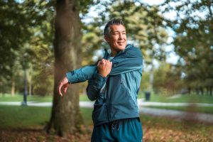 Asian man in track suit stretching his arm in a wooded park