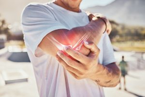 Close up photo of a man in a t-shirt massaging his elbow. Digital imaging of the bone structure of the arm is overlaid.