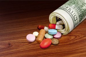 A variety of pills spilling out from the center of a rolled stack of dollars.
