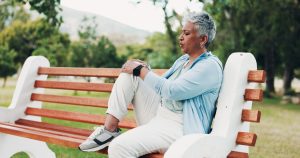 Knee pain, fitness and mature woman in park with injury, muscle strain and inflammation on bench. Nature, sports and senior person with accident for exercise, workout and walking outdoors for health