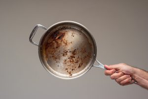 Dirty oily burnt metal frying pan held in hand by male hand.