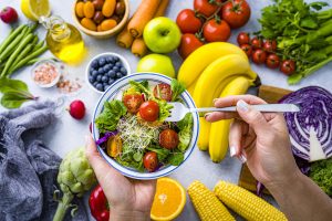 Woman eating fresh rainbow colored salad. Multicolored fruits and vegetables background. Healthy eating and dieting concept.