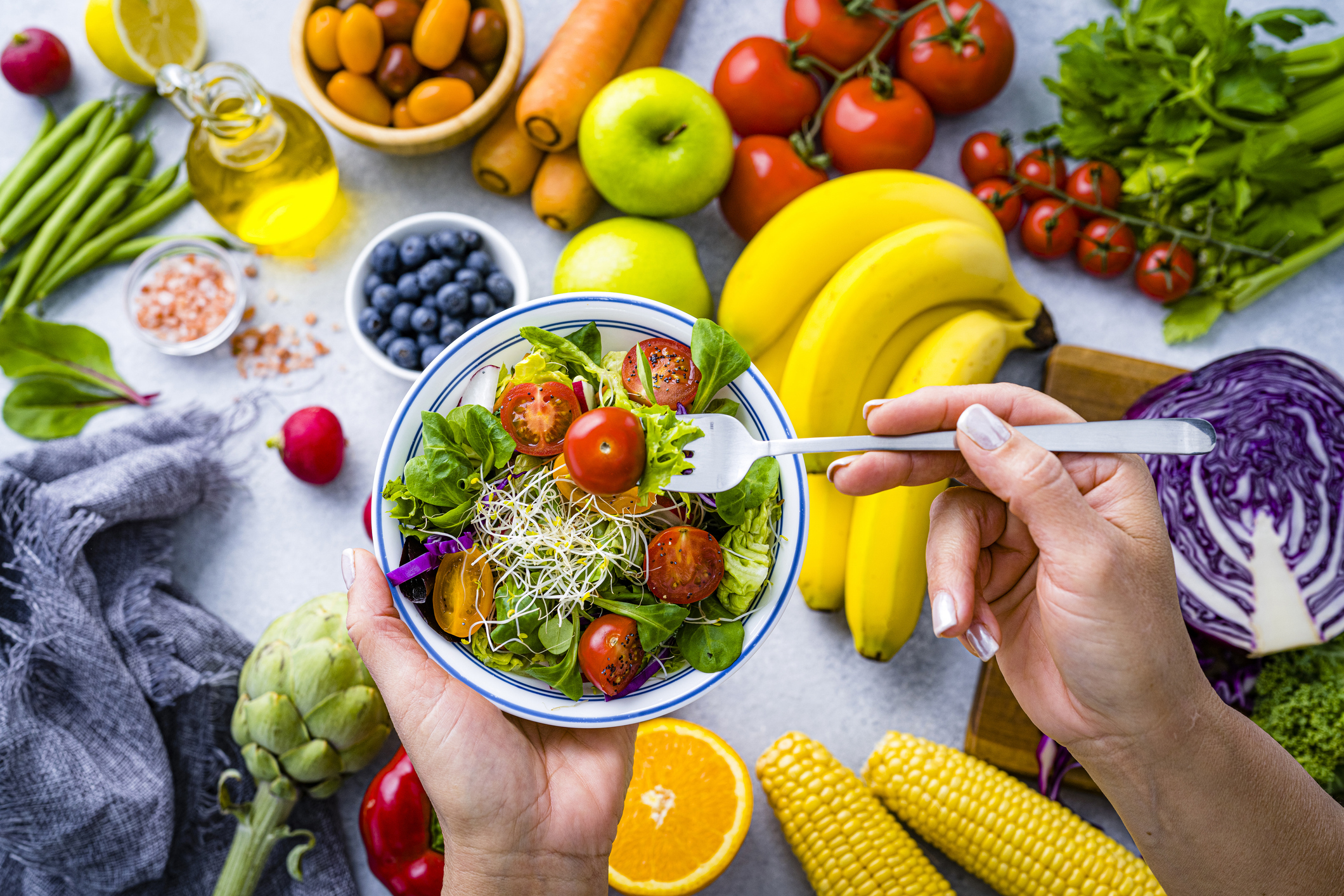 Woman eating fresh rainbow colored salad. Multicolored fruits and vegetables background. Healthy eating and dieting concept.
