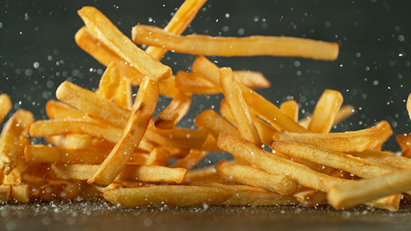 A close up of French fries and salt falling onto a table.