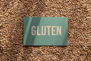A paper with "gluten" written on it, resting on top of a background of wheat grains.