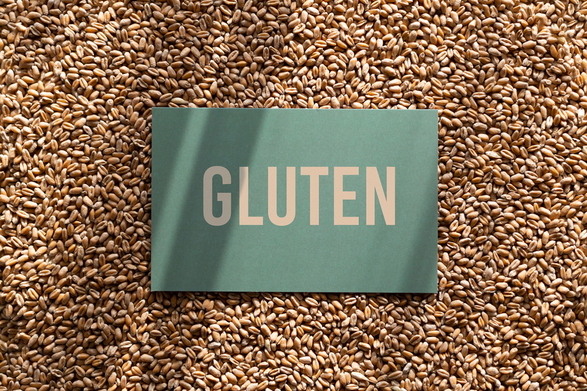 A paper with "gluten" written on it, resting on top of a background of wheat grains.