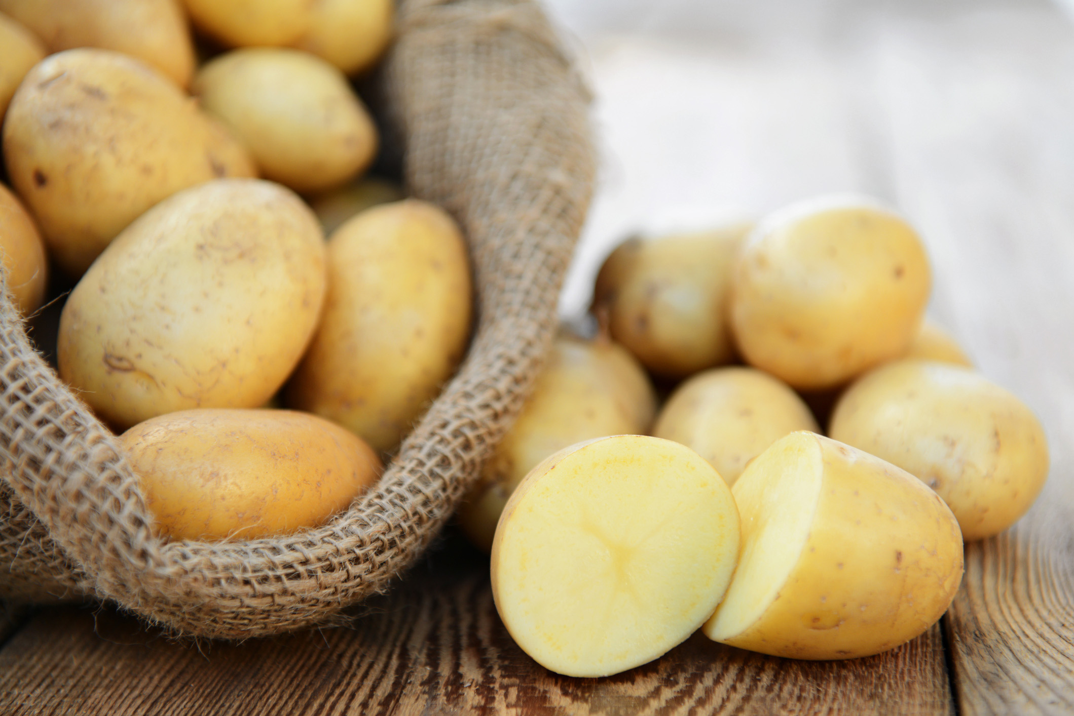 A pile of halved raw potatoes resting beside a burlap bag filled with whole potatoes.