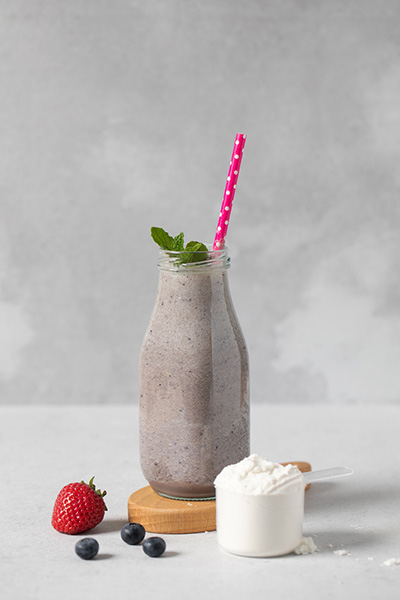 Healthy berry smoothie with protein and scoop of protein, fresh mint and strawberries on a wooden board