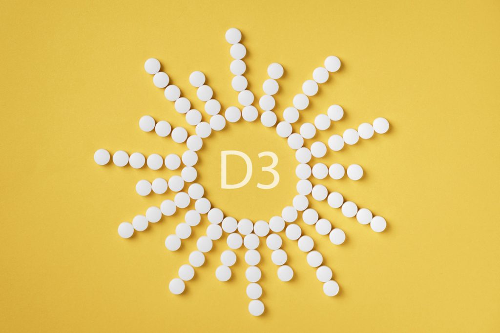 Pills of vitamin D3 in a shape of sun on yellow background.