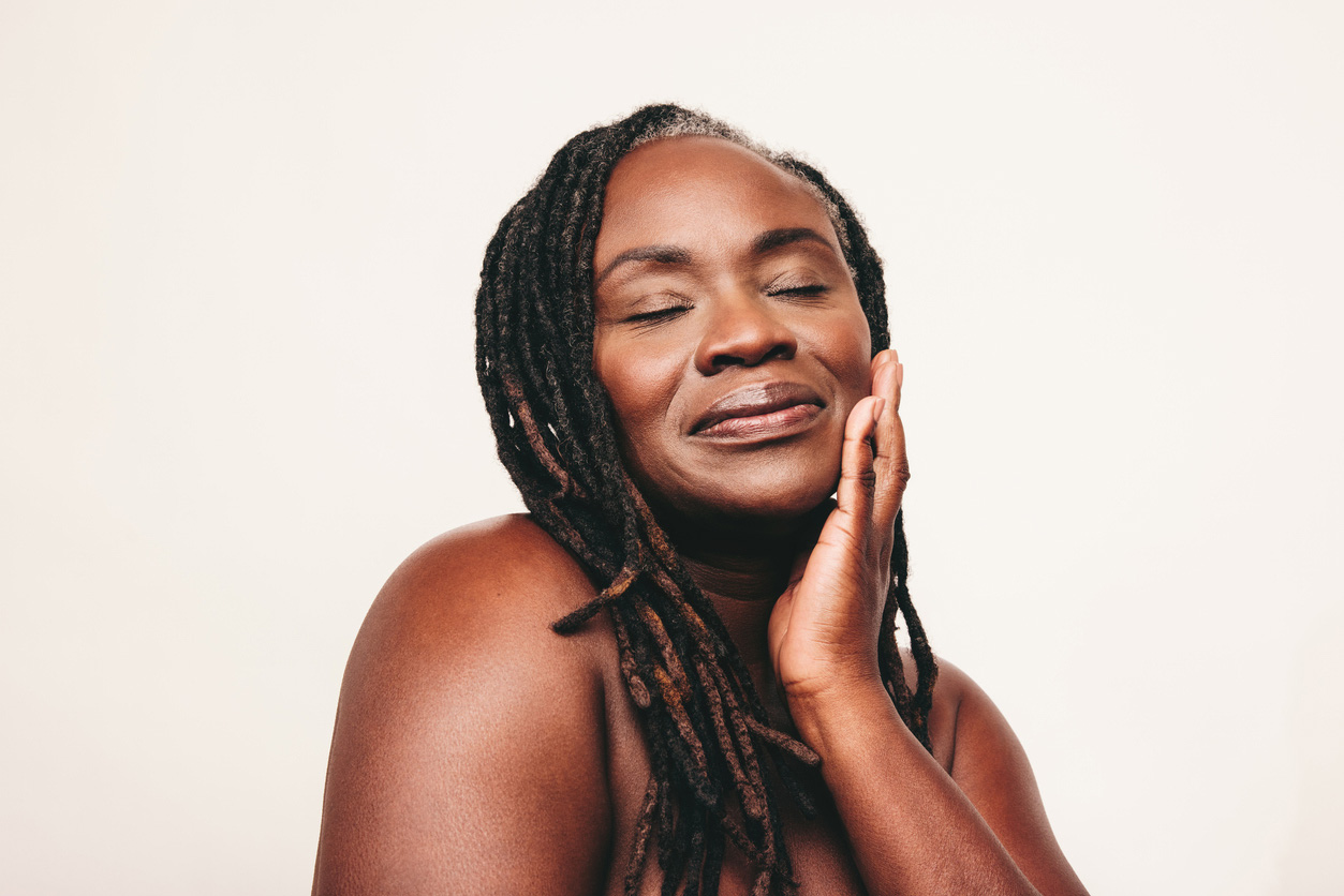 Beautiful woman with dreadlocks touching her flawless skin with her eyes closed. Mature Black woman ageing gracefully.