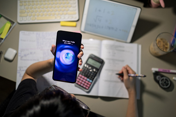 A student interacts with an AI chatbot on a smartphone while studying with a calculator, notebook, and digital tablet on a desk.