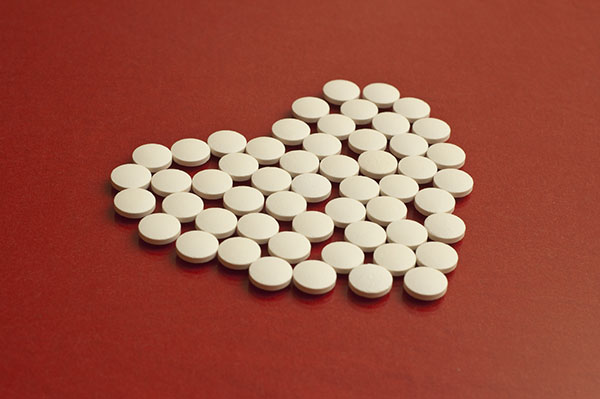 White heart medication tablets arranged into a heart shape on a red background