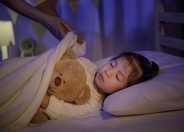 Little girl and her teddy bear being tucked into bed