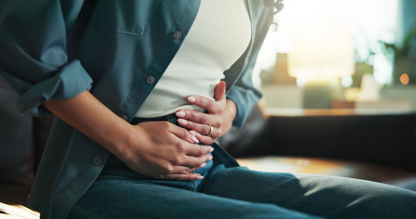 Close up of a woman holding her hands against her midsection while experiencing digestive upset