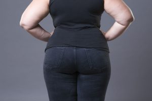 Plus size caucasian woman in a black t-shirt and blue jeans, viewed from behind with her hands on her hips