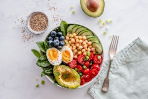 Overhead view of a healthy meal bowl with avocado, chickpeas, egg, veggies and blueberries