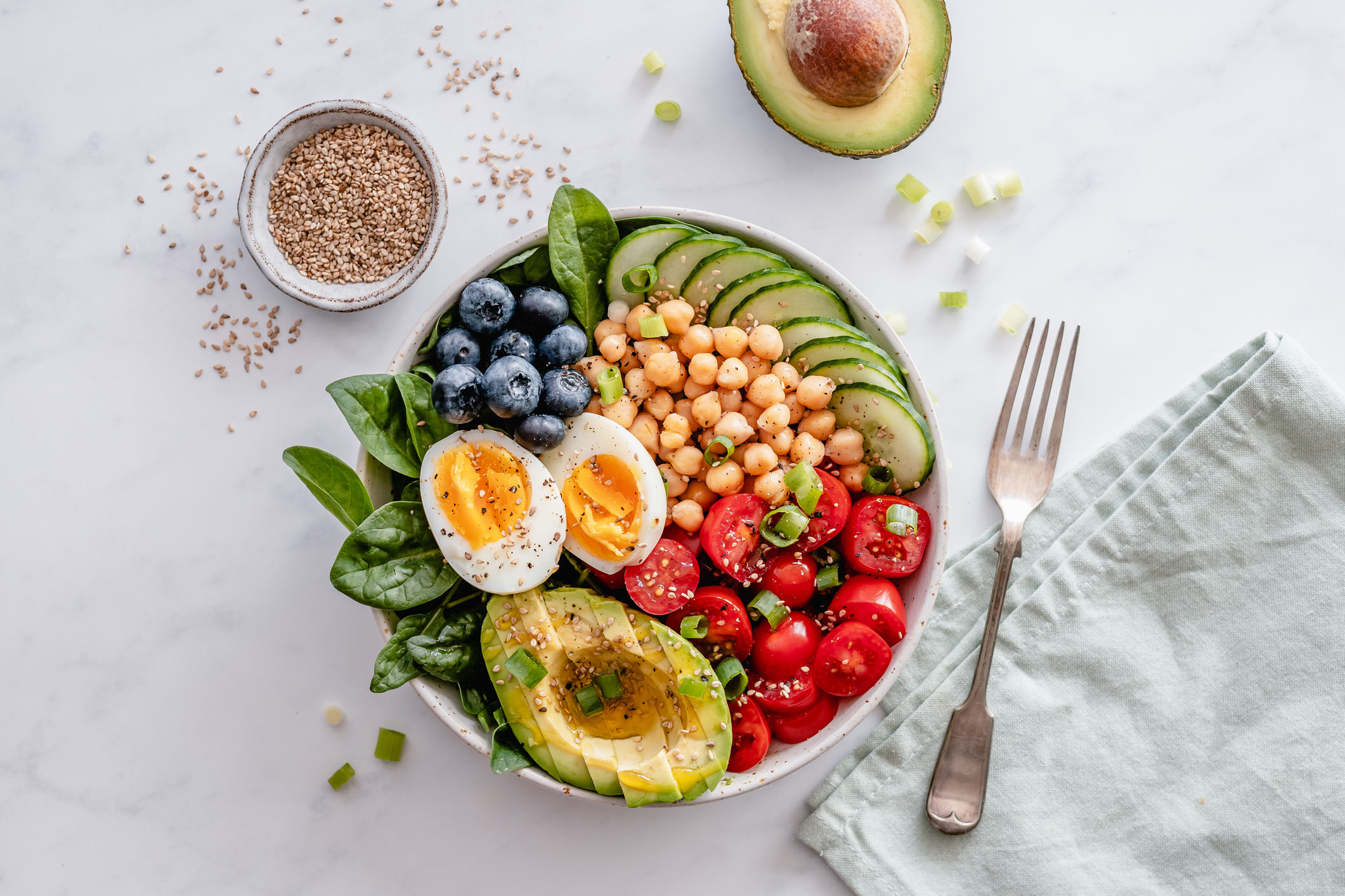 Overhead view of a healthy meal bowl with avocado, chickpeas, egg, veggies and blueberries