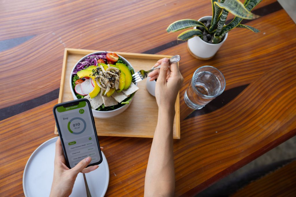 Using mobile app checking calories while eating vegan salad cooked by fresh ingredients during morning routine.