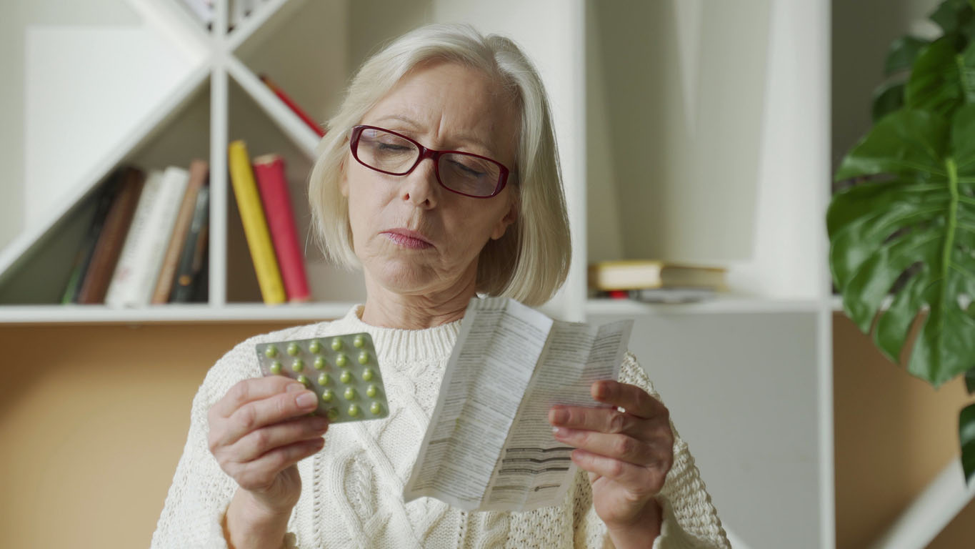 Senior woman reading the instructions for a medication in blister packs.