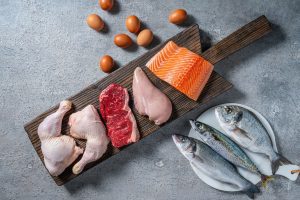 Healthy protein source food meat, eggs and fish: chicken, beaf, salmon, seabass, mackerel and sea bream on a cutting board in a gray kitchen table background