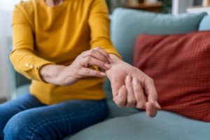 Senior woman sitting on a couch and scratching her arm, indicating skin irritation or allergy discomfort