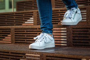Woman in jeans and white sneakers walking down steps.