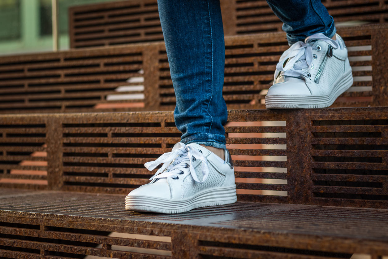 Woman in jeans and white sneakers walking down steps.