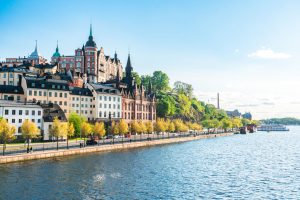 Scenic view of the stockholm waterfront, showcasing colorful buildings, lush trees, and a clear blue sky, capturing the essence of the city's charm