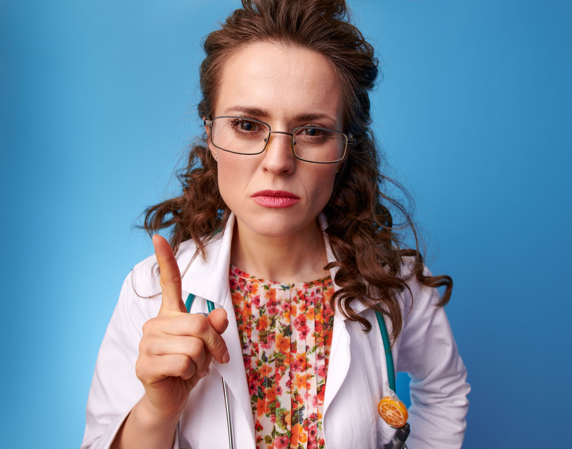 Woman doctor in white medical robe threatening with finger isolated on blue