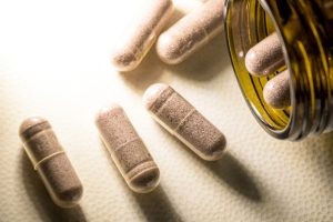 This macro shot features a collection of herbal supplement capsules, some spilling out of an amber-colored glass bottle.