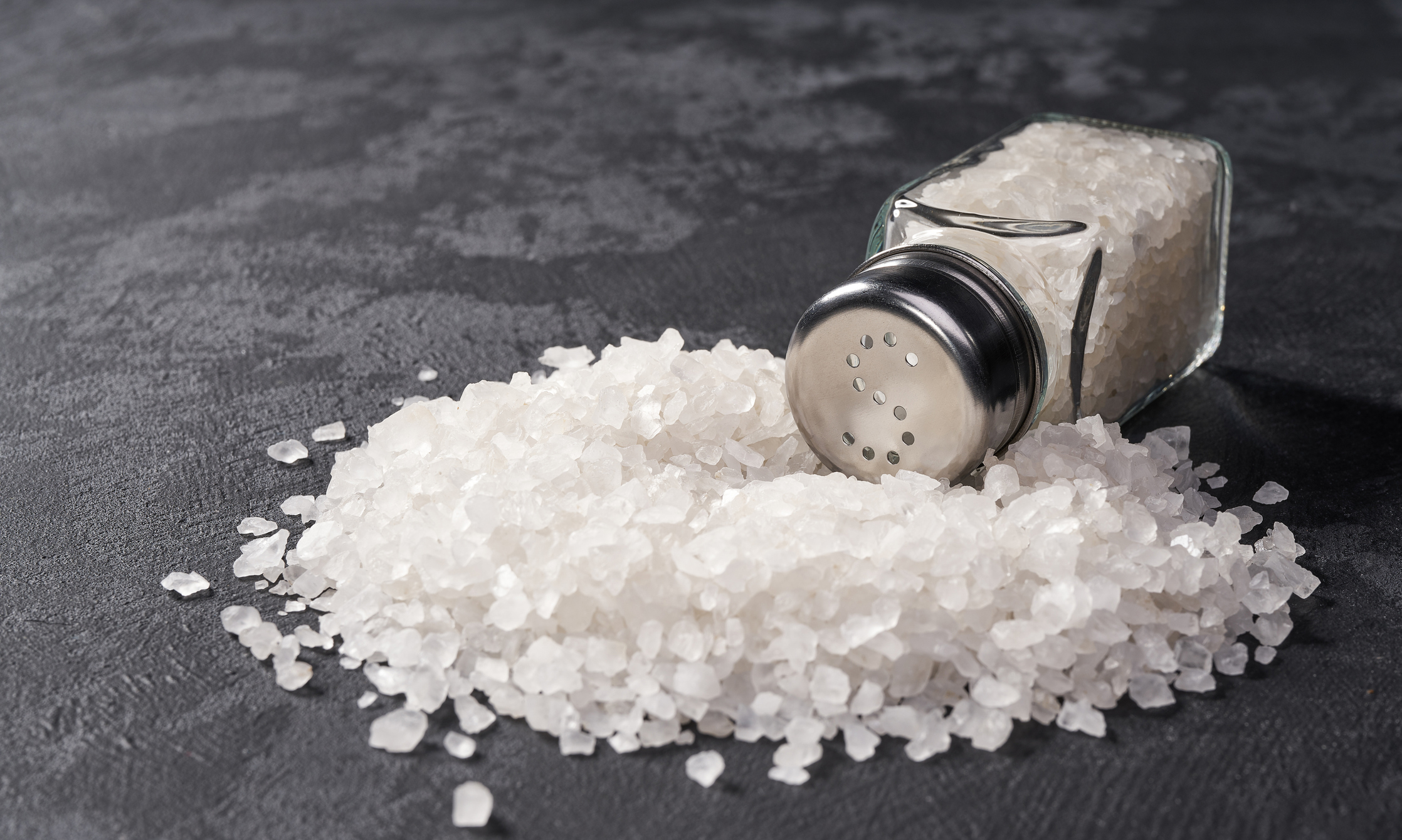Pile of salt and salt shaker on black table